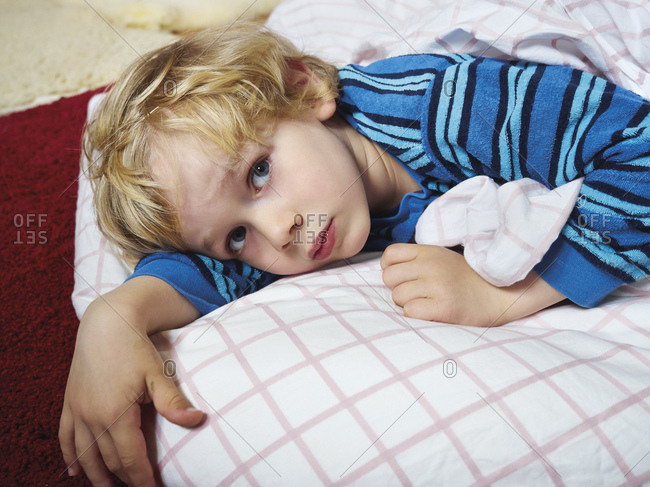 Portrait of little boy lying on the floor with bedding