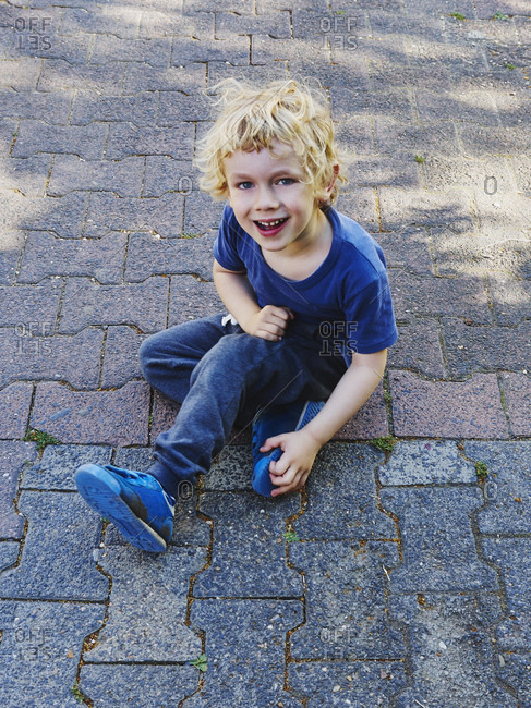 Portrait of smiling little boy dressed in blue sitting on pavement