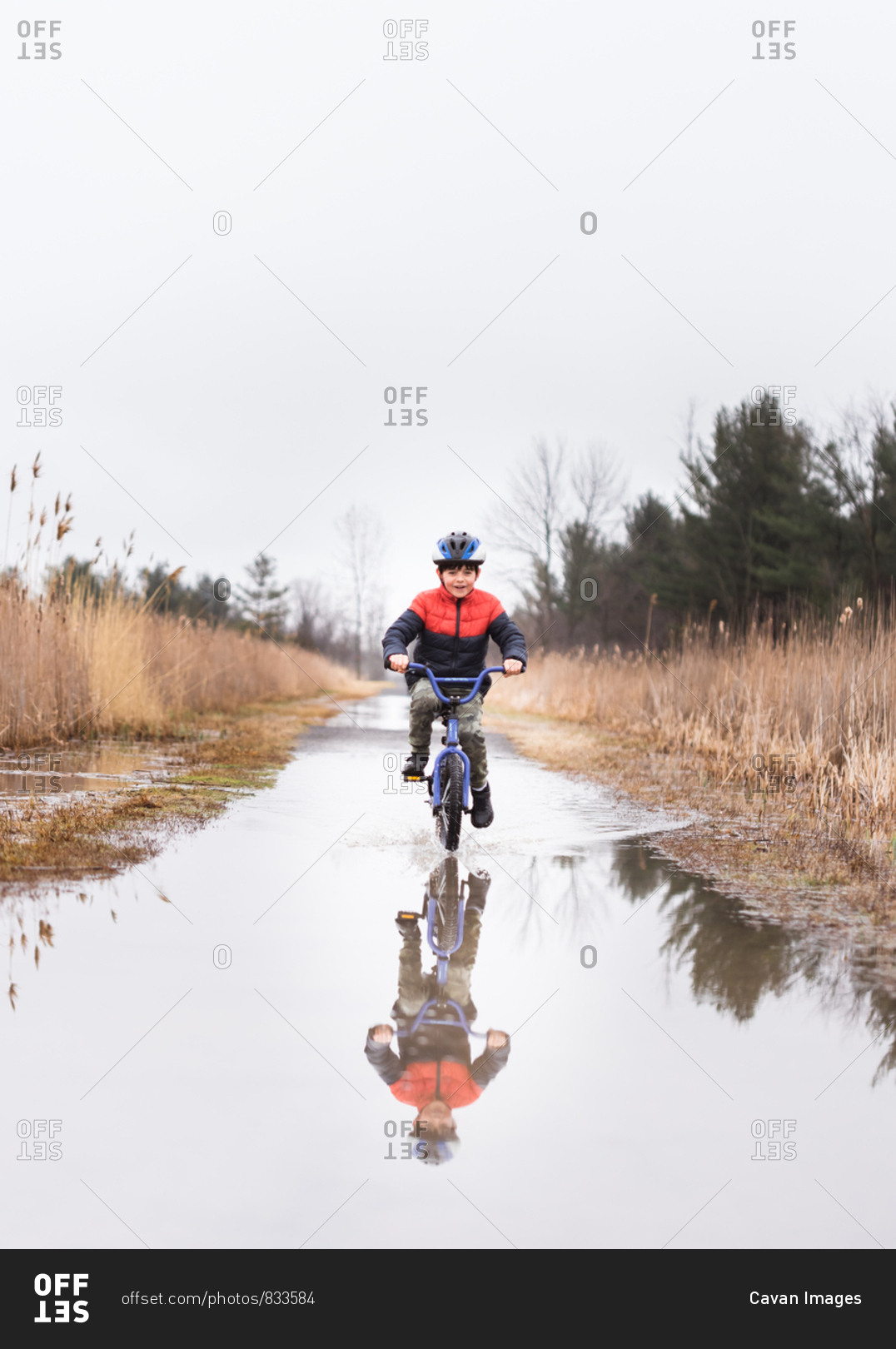Young boy riding his bike through a puddle on a flooded trail.