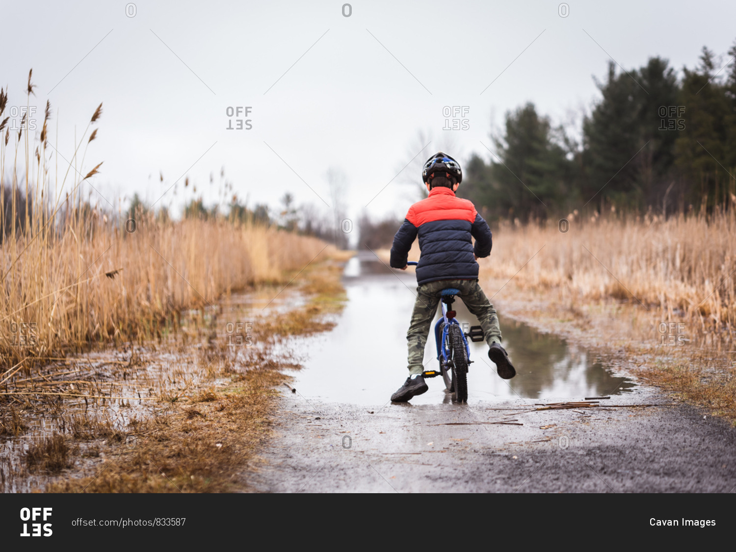 Young boy riding his bike through a large puddle on a flooded trail.