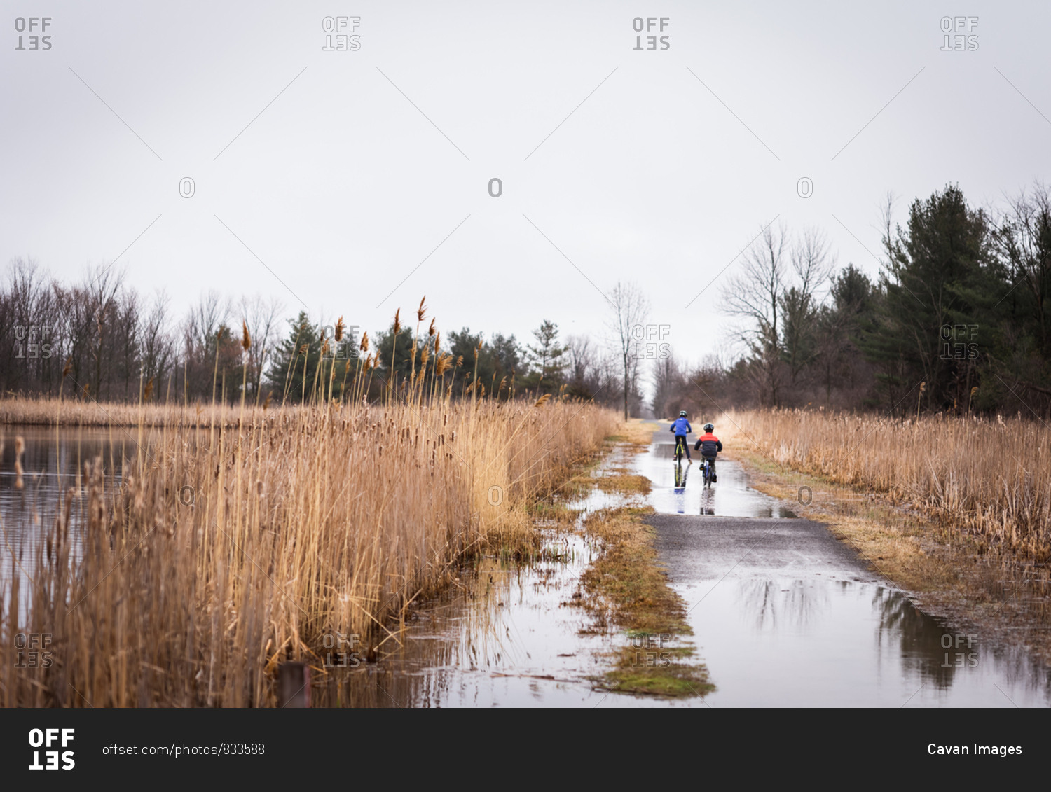 Two boys riding their bikes through a large puddle on a flooded trail.