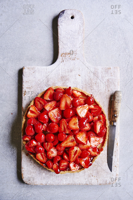 A strawberry tart piled high with strawberries on a board and knife on the side.