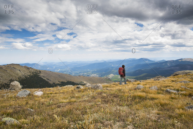 A Woman Walks Across A Field Towards The Mountains In Colorado