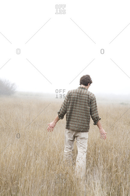 A young man walks with arms out in a field of tall grasses, California.
