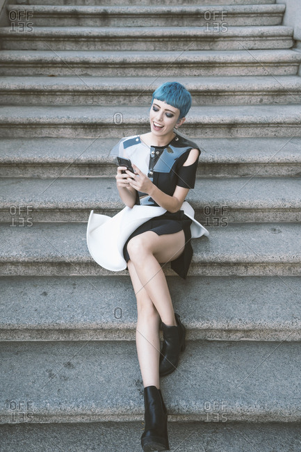 From above of young female with short blue hair and in trendy futuristic  dress listening to music with phone on street steps Stock Photo - Alamy