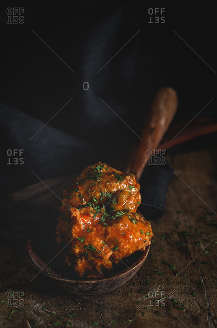 From above appetizing meatballs in brown wooden ladle on black striped towel