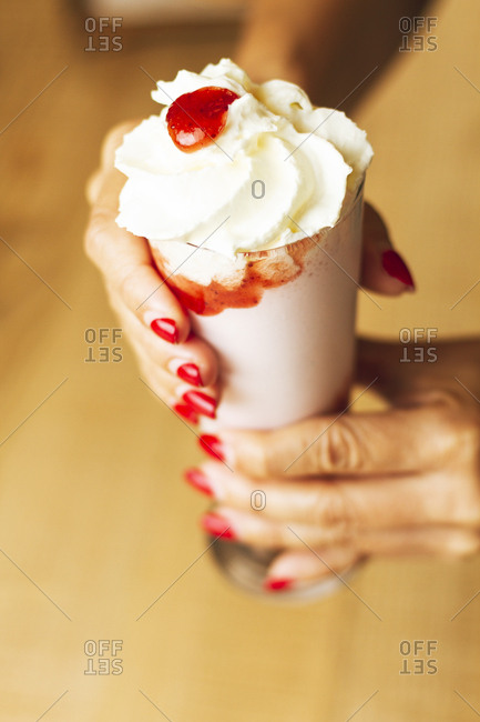 From above tasty ice cream decorated with red juicy in paper cone in hands with ideal manicure