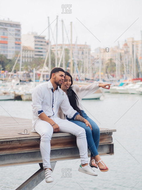 Young lovely couple sitting on dock with feet and embracing looking along