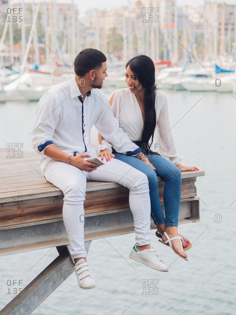 Young lovely couple sitting on dock with feet and embracing looking at each other