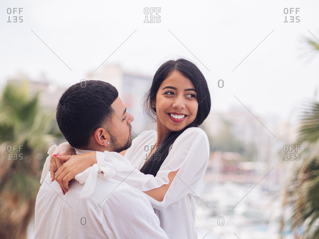 Side view of lovely young couple in light clothes bonding and hugging with love and tenderness on dock in port