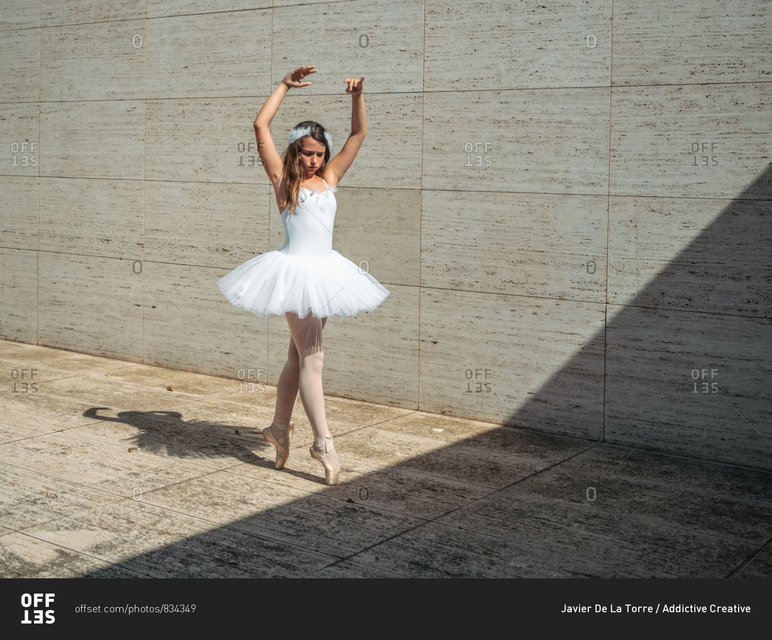 Ballerina in white ballet tutu performing exercises in classroom in contrast sunny light