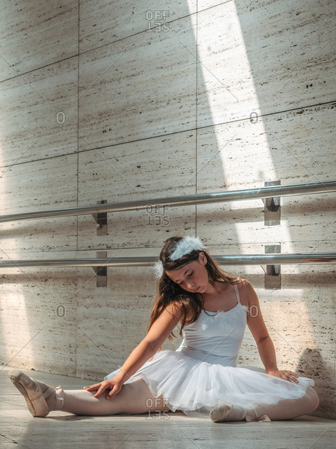 Ballerina sitting on floor stretching graceful leg in classroom
