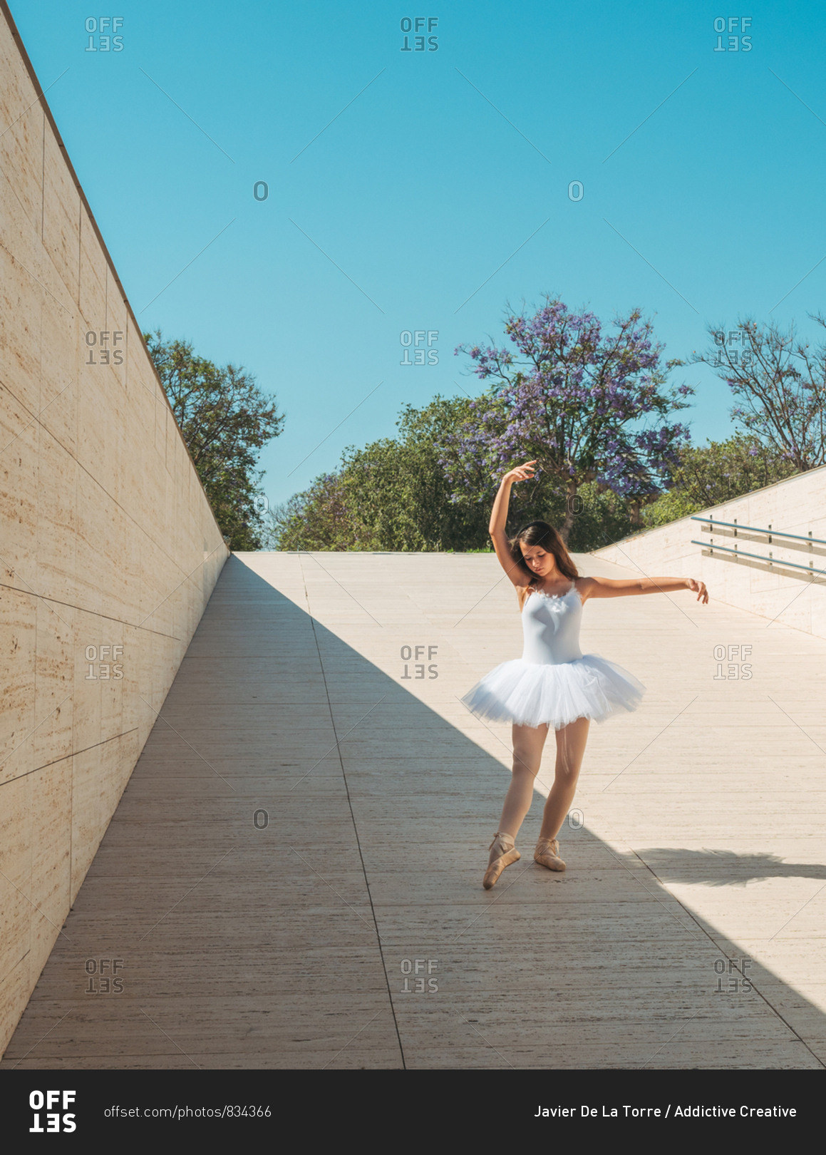 Classical ballet position gracefully performing by ballerina with raising hands and stretching legs outside in bright sunny day