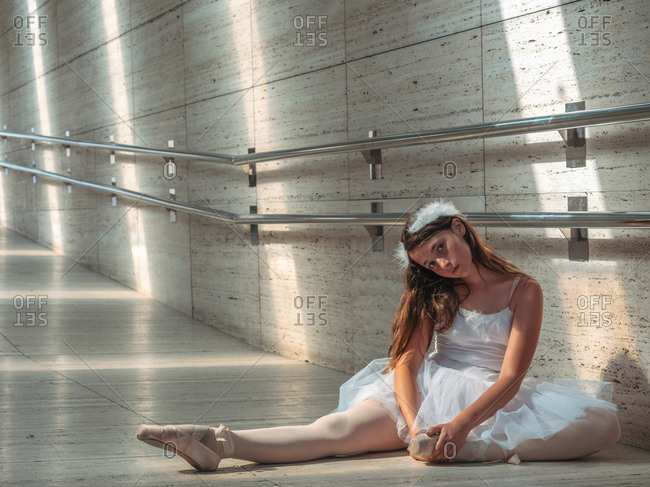 Ballerina sitting on floor stretching graceful leg in classroom
