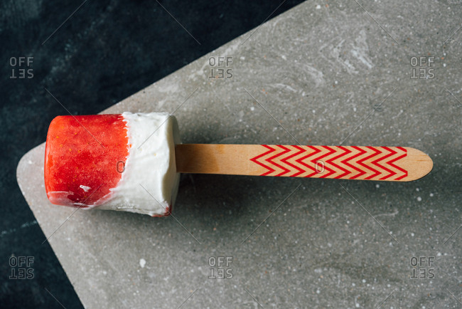 Close-up view of watermelon and cream popsicle laying on fancy plate on dark background