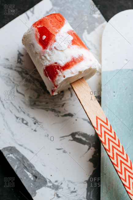 Close-up top view of watermelon and cream popsicle laying on fancy dish on dark background