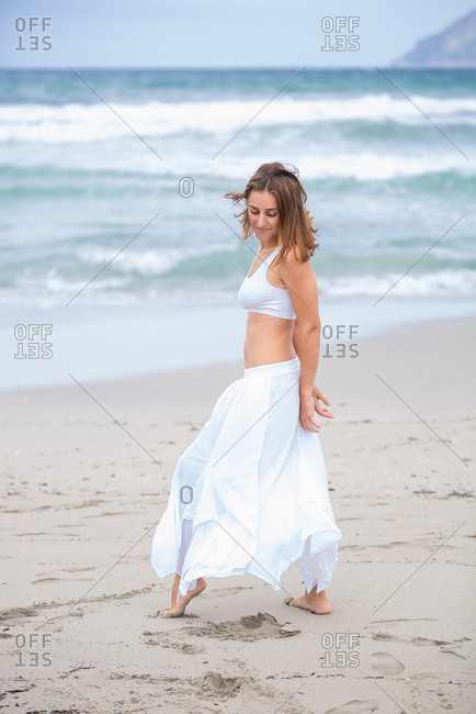 Side view of beautiful attractive female in white outfit dancing on sand near waving sea