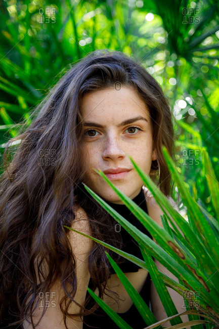 Attractive brunette woman sitting in tropical bushes and looking at camera