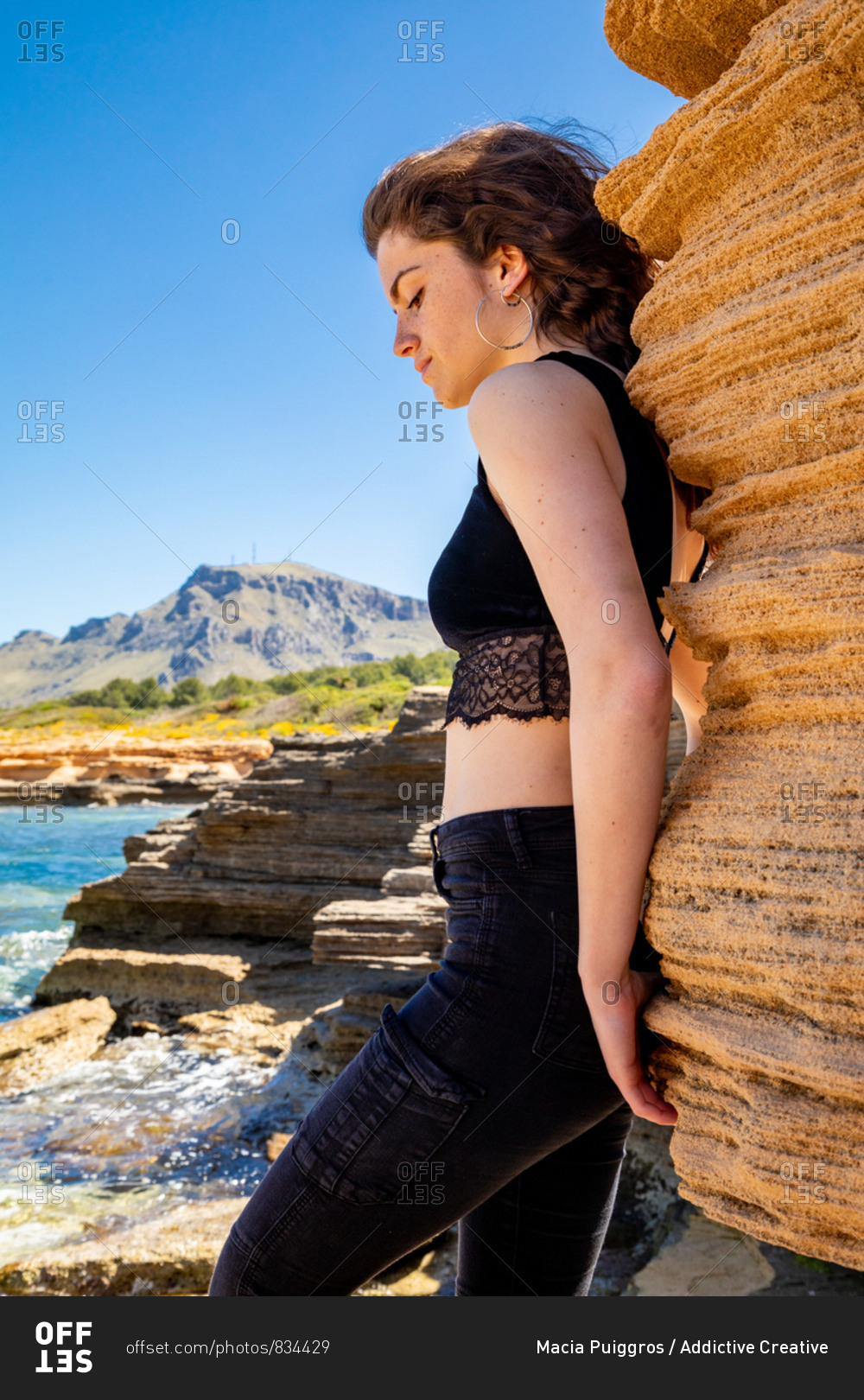Side view of slim woman in black crop top and jeans standing in canyon and enjoying landscape