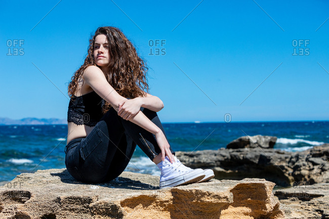 Side view of pretty young woman resting on cliff looking away on sunny day