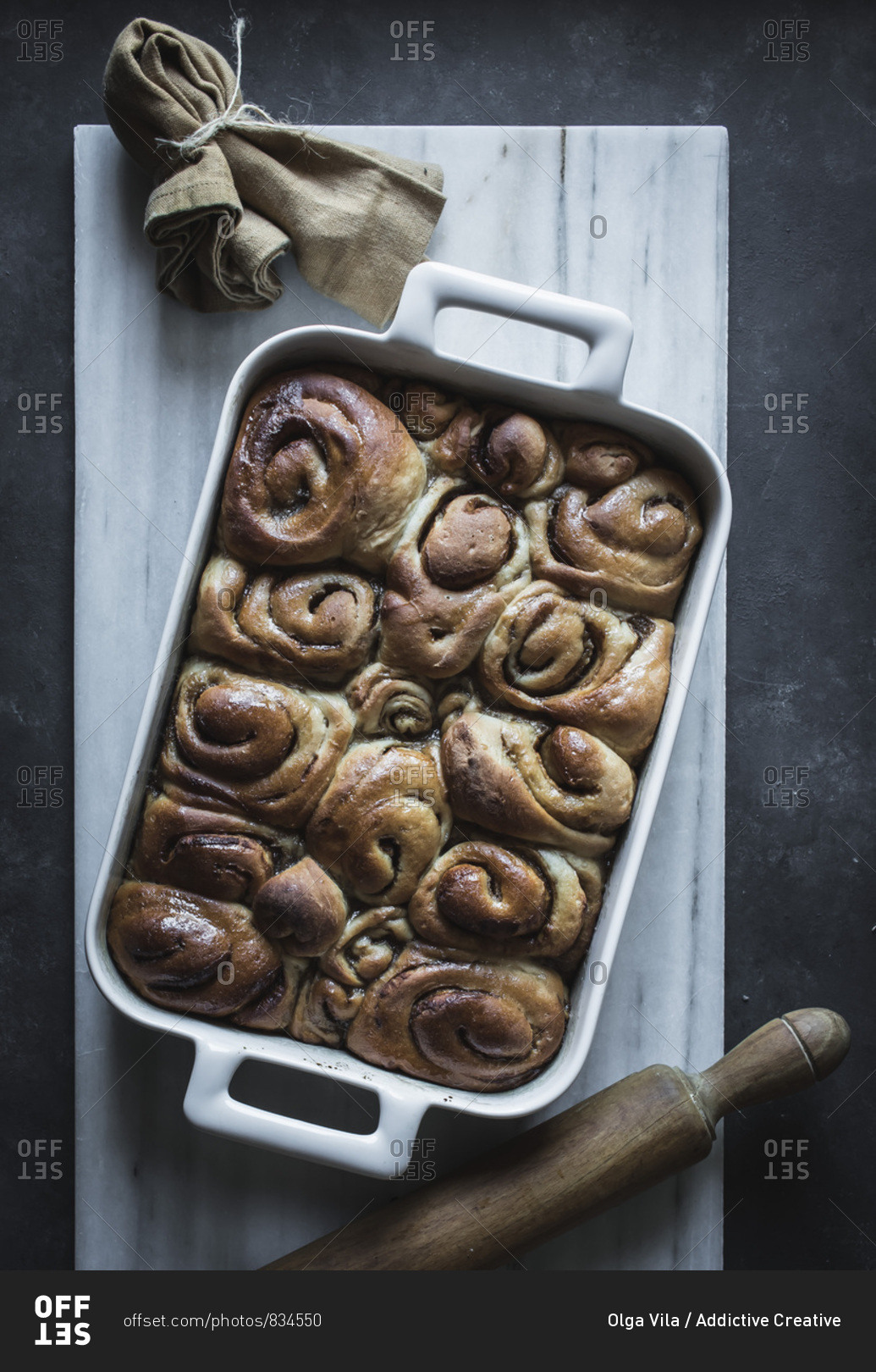 From above tray with fresh homemade cinnamon buns and wooden rolling pin on white marble board