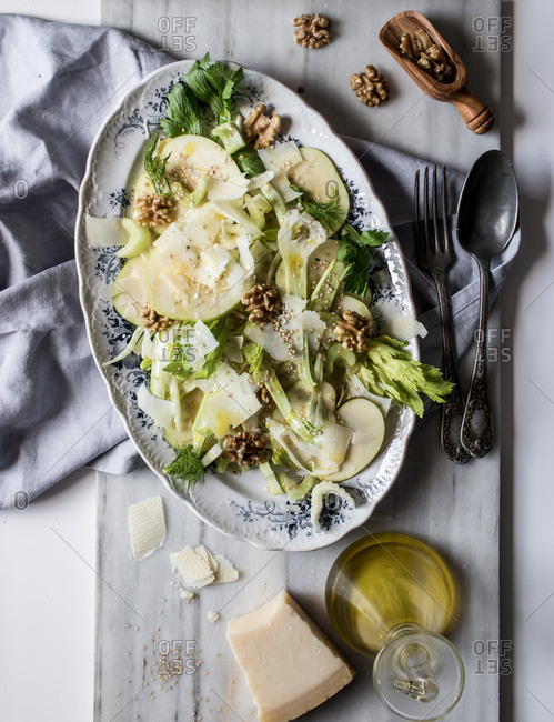 From above dish with delicious salad made of apples, parmesan cheese, walnuts, celery and oil on white background