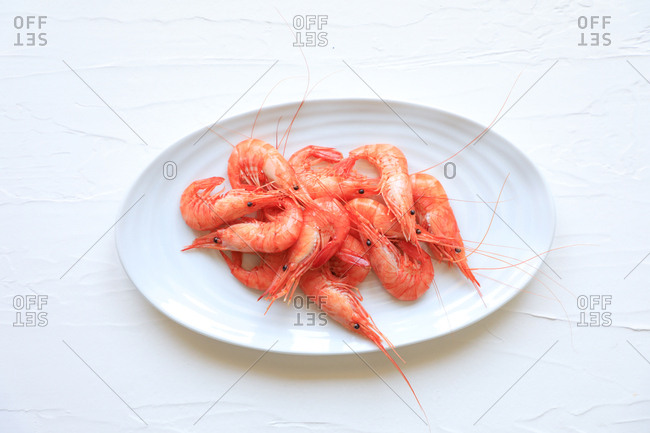 From above cooked pink shrimps arranged on oval dish against white texture background