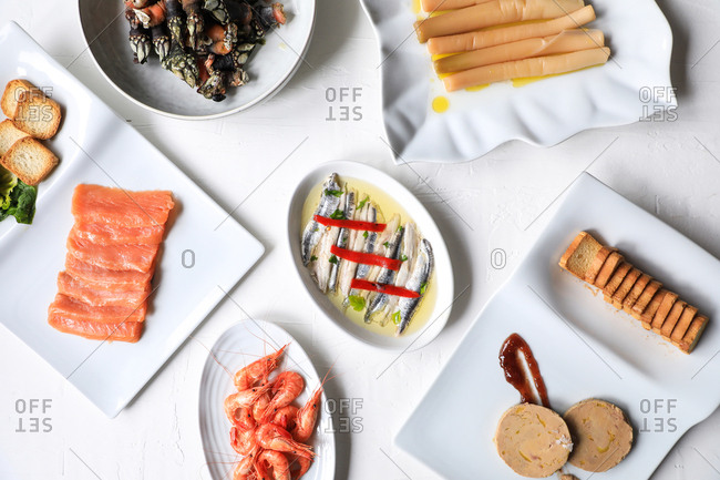 From above appetizing meal with cooked shrimps, salmon, marinated fish and toasts arranged on white background