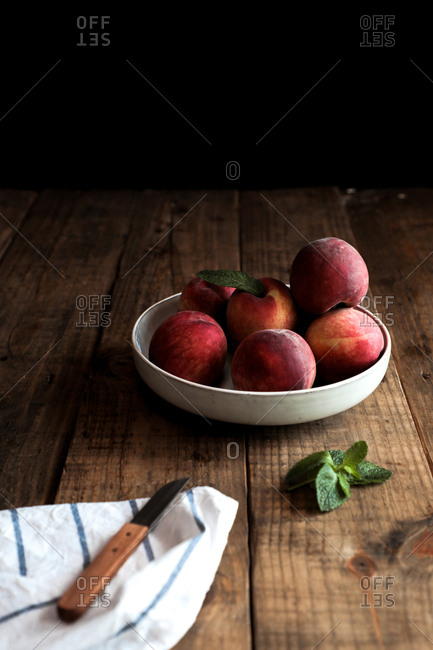 Appetizing bright peaches with leaves in white plate on wooden table and knife on cloth napkin