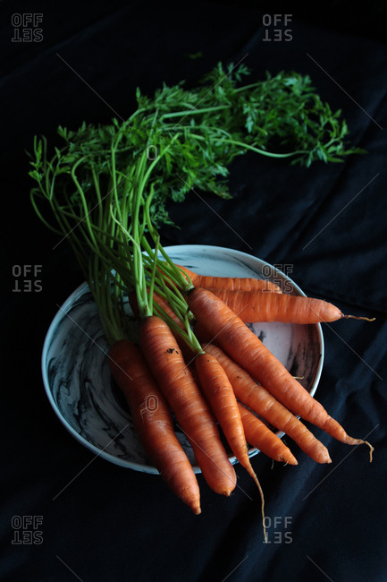 From above appetizing crispy orange carrot with green lush stems on white plate on black background