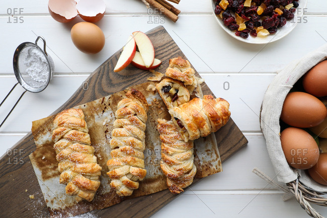 From above delicious fresh strudels with sweet apples and raisins placed on white tabletop near sieve and raw eggs