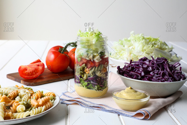Yummy pasta with fresh vegetables and sauce placed inside jar on white table
