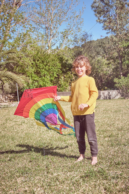 Happy kid playing with colorful kite flying in blue sky on nature background