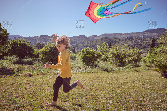Happy kid playing with colorful kite flying in blue sky on nature background