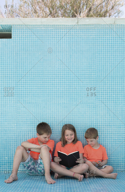 Children sitting in empty pool and reading book