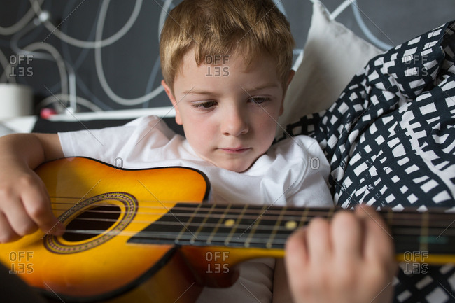 Young blonde boy playing toy guitar