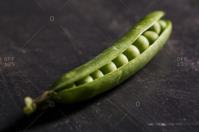 Peeled fresh peas and pea pods on dark background
