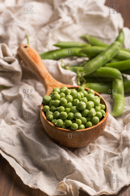Fresh peas in a wooden scoop placed in a clear cloth on a wooden table