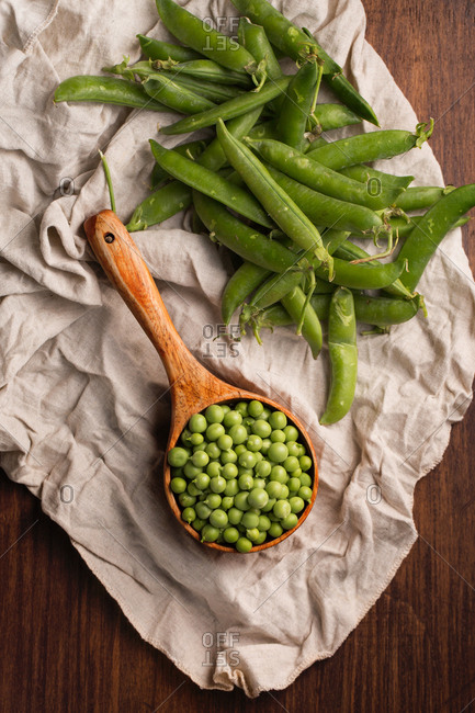 Fresh peas in a wooden scoop placed in a clear cloth on a wooden table