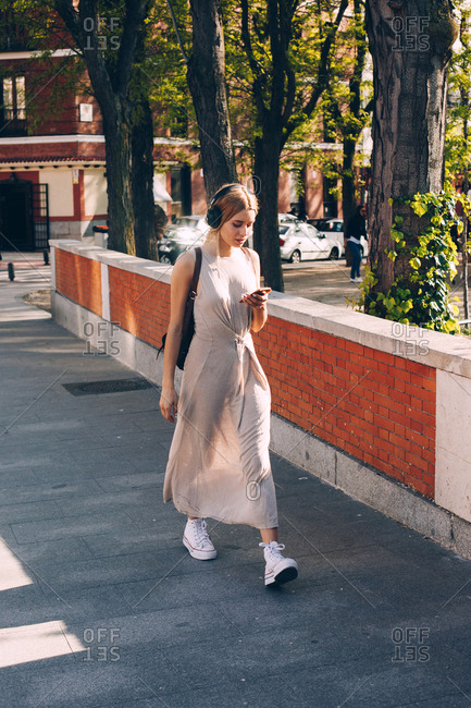 Attractive woman in long summer dress listening music during walking on street in daylight