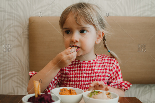 Cute little girl eating assorted tasting appetizing snack at table