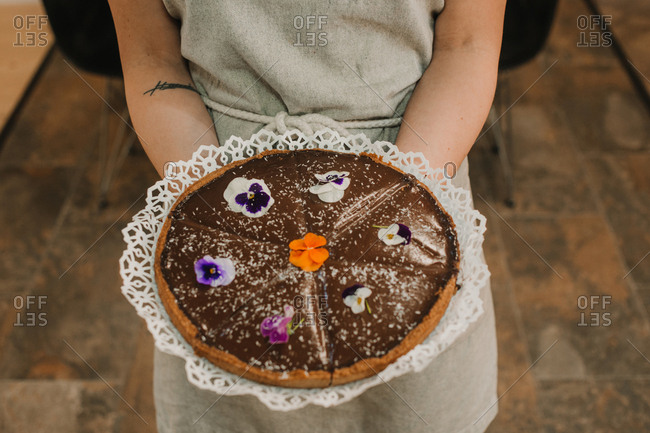 From above tasty appetizing cake festively decorated with bright flowers in hands of woman