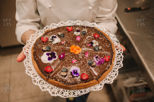 From above tasty appetizing cake festively decorated with bright flowers in hands of woman