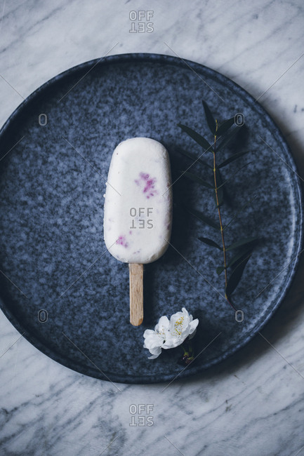 Top view still life of creamy raspberry popsicle placed on dark dish on top of marble surface and decorated with flowers
