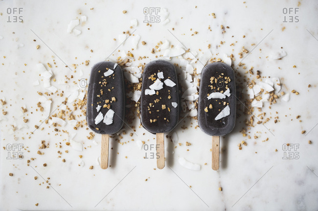 Top view of assorted chocolate ice cream popsicles covered with different toppings on a marble surface