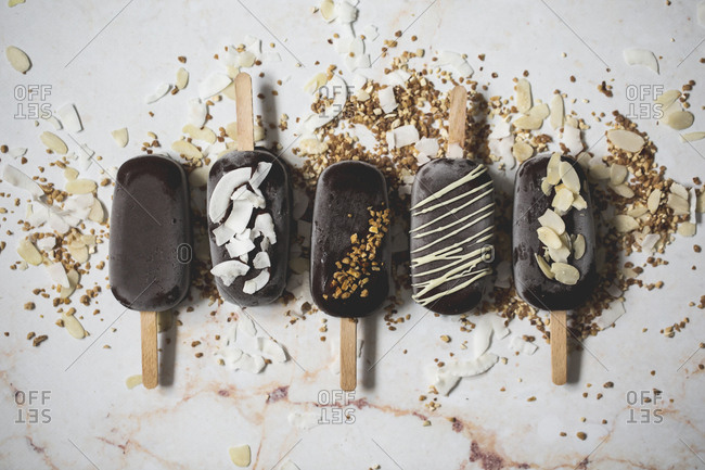 Top view of assorted chocolate ice cream popsicles covered with different toppings on a marble surface