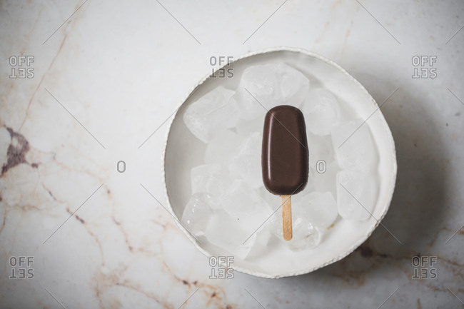 Top view of chocolate ice cream popsicle in a bowl with ice cubes placed on a marble surface