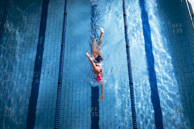 High angle view of a Caucasian woman wearing a pink swimming cap and goggles doing a freestyle stroke in a swimming pool