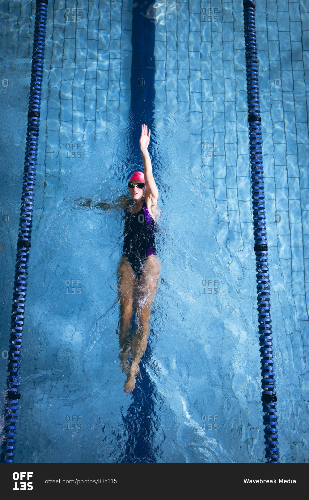 High angle view of a Caucasian woman wearing a pink swimming cap and goggles doing a back stroke in a swimming pool