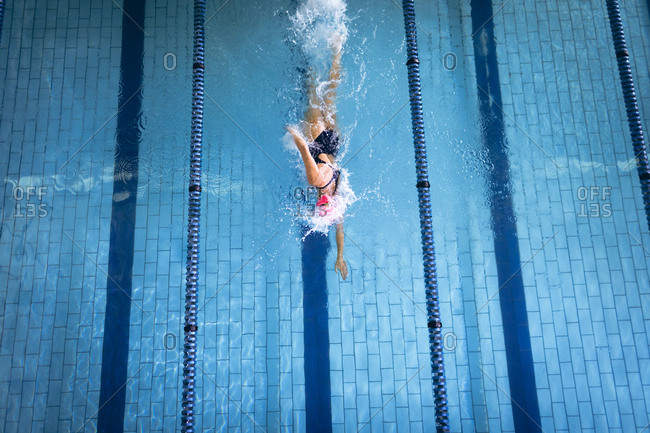 High angle view of a Caucasian woman wearing a swimsuit and a pink swimming cap doing freestyle stroke in the swimming pool